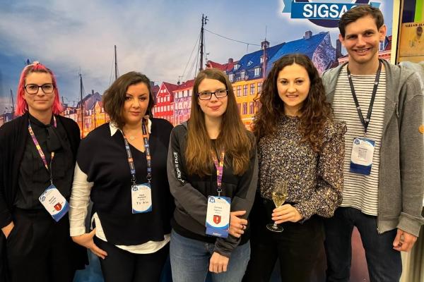 Photo of the group of TUW researchers in front of the banner of the ACM Conference on Computer and Communications Security featuring Martina Lindorfer, Elena Andreeva, Carlotta Tagliaro, Sophie Rain, and David Schmidt from left to right