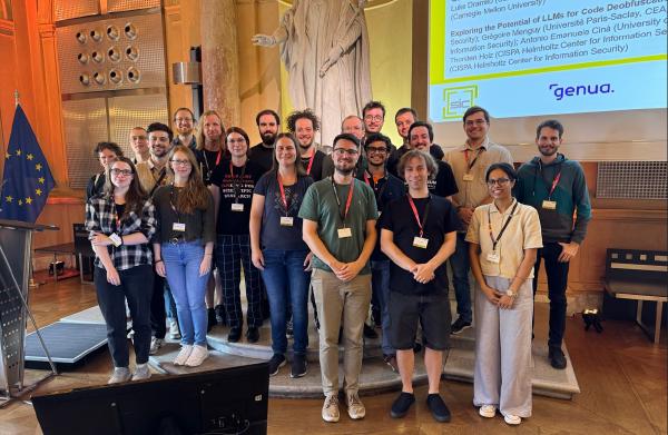 A group photo of around 20 participants standing together inside a historic hall with a European Union flag on the left and a large statue in the background